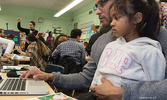 A father and daughter using a computer to look at a savings tracker during the Savings Tracker launch at PS 2.